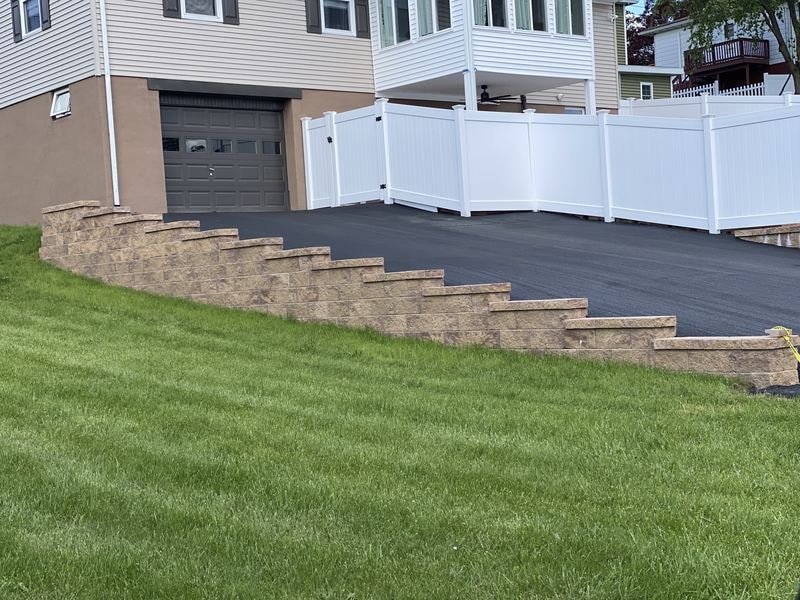 Driveway with white vinyl privacy fence and block retaining wall